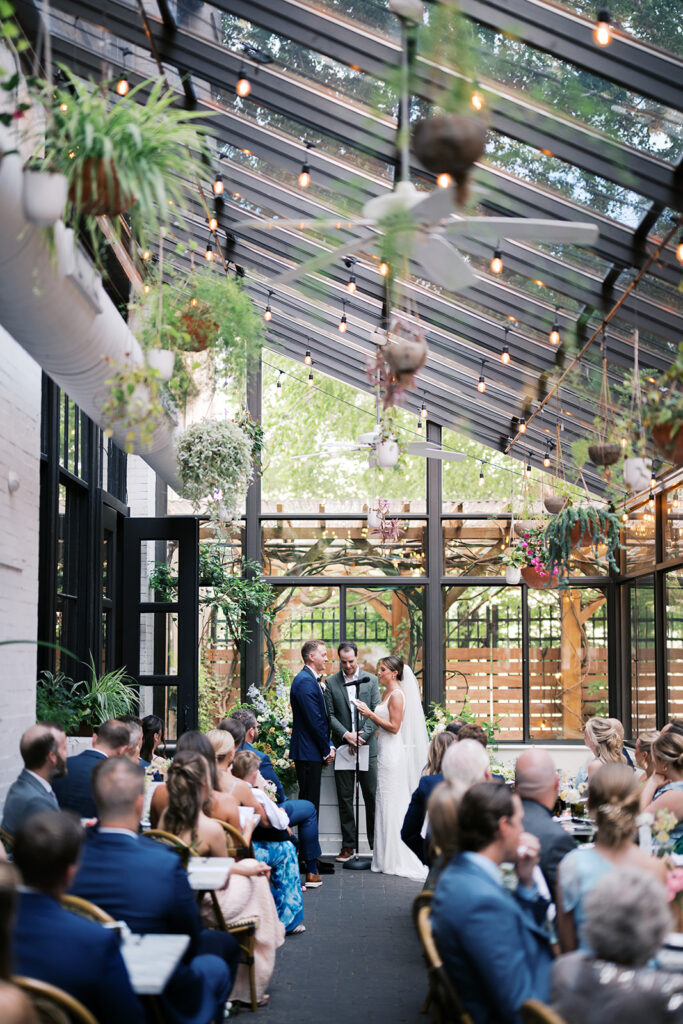 Birde and groom exchange vows in front of guests inside the glass patio at Osteria restaurant in Philadelphia | Lindsey Ford Photography