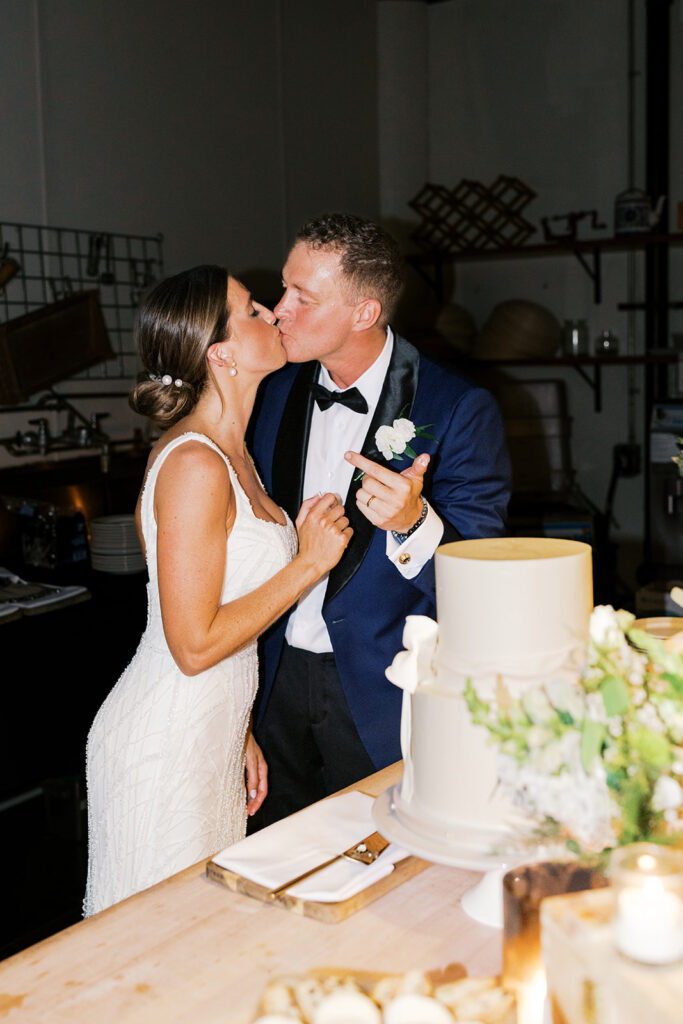 Bride and groom kiss behind two tier white wedding cake at Osteria in Philly