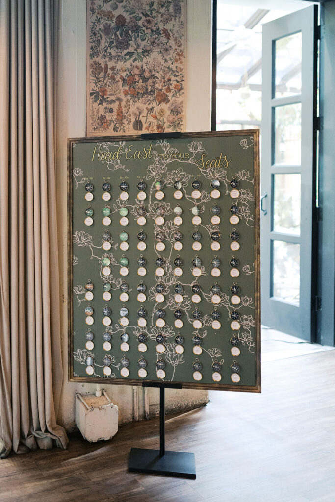 Seating chart board covered with small compasses with wedding guest names written in script font for a wedding at Osteria in Philly
