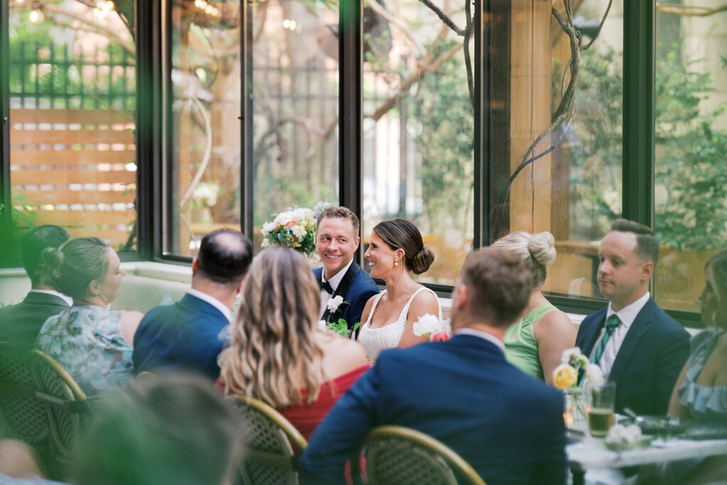 Bride and groom sit at a table and laugh while surrounded by their wedding guests at Osteria in Philly