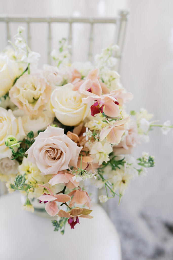 Soft pastel wedding bouquet with yellow, pink, and white flowers sits on a white chair