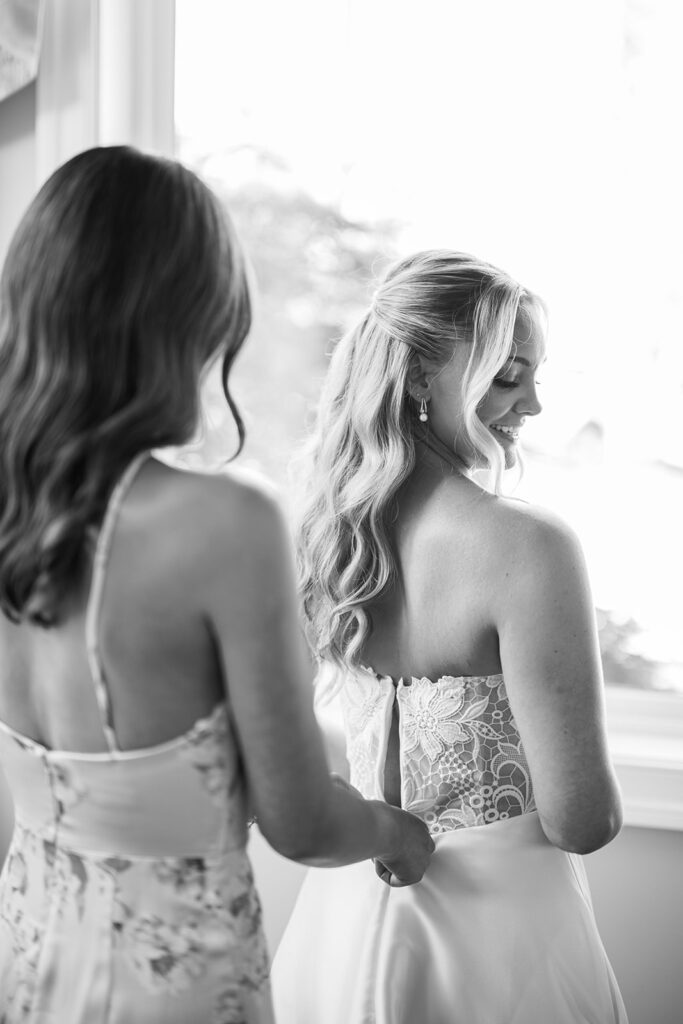 Bridesmaid zips up brides lace back wedding dress