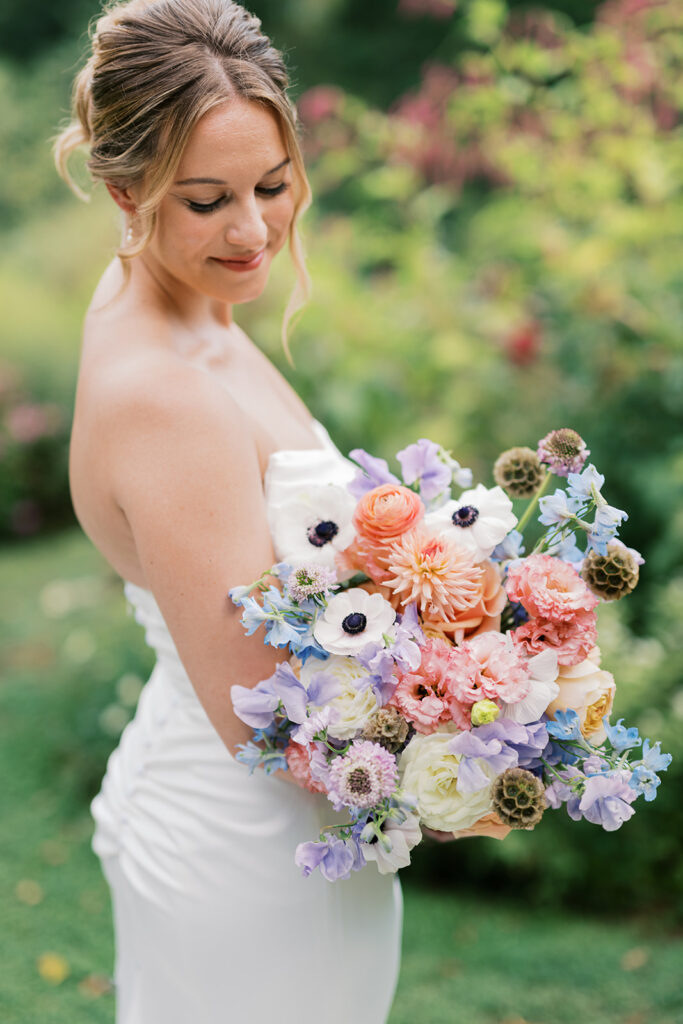 Bride holds lush wedding bouquet full of blue, lilac, pink, and peach colored florals at Bartram's Gardens
