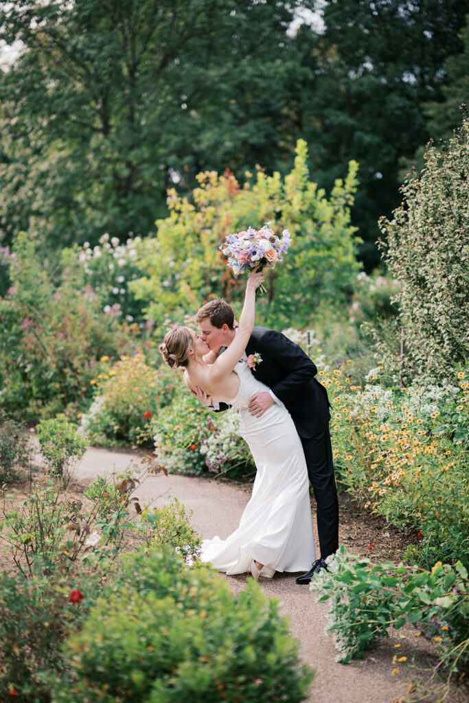 Groom dips bride for a kiss surrounding by floral landscaping during their wedding portraits at Bartram's Garden by Lindsey Ford Photography