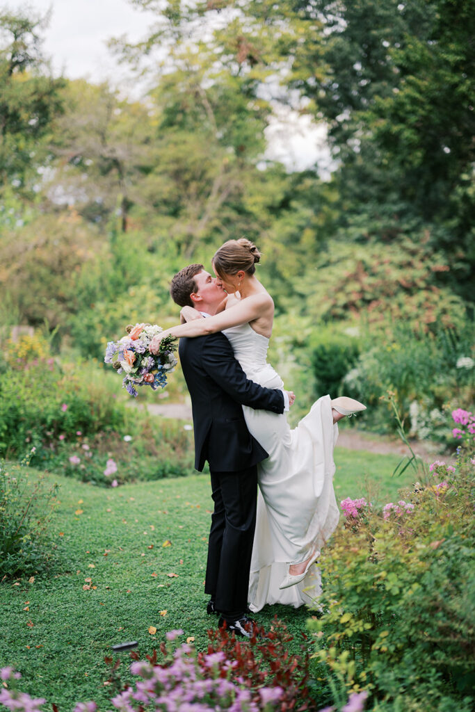 Groom lifts bride in the middle of a flower garden during their wedding portraits at Bartram's Garden by Lindsey Ford Photography in Philadelphia