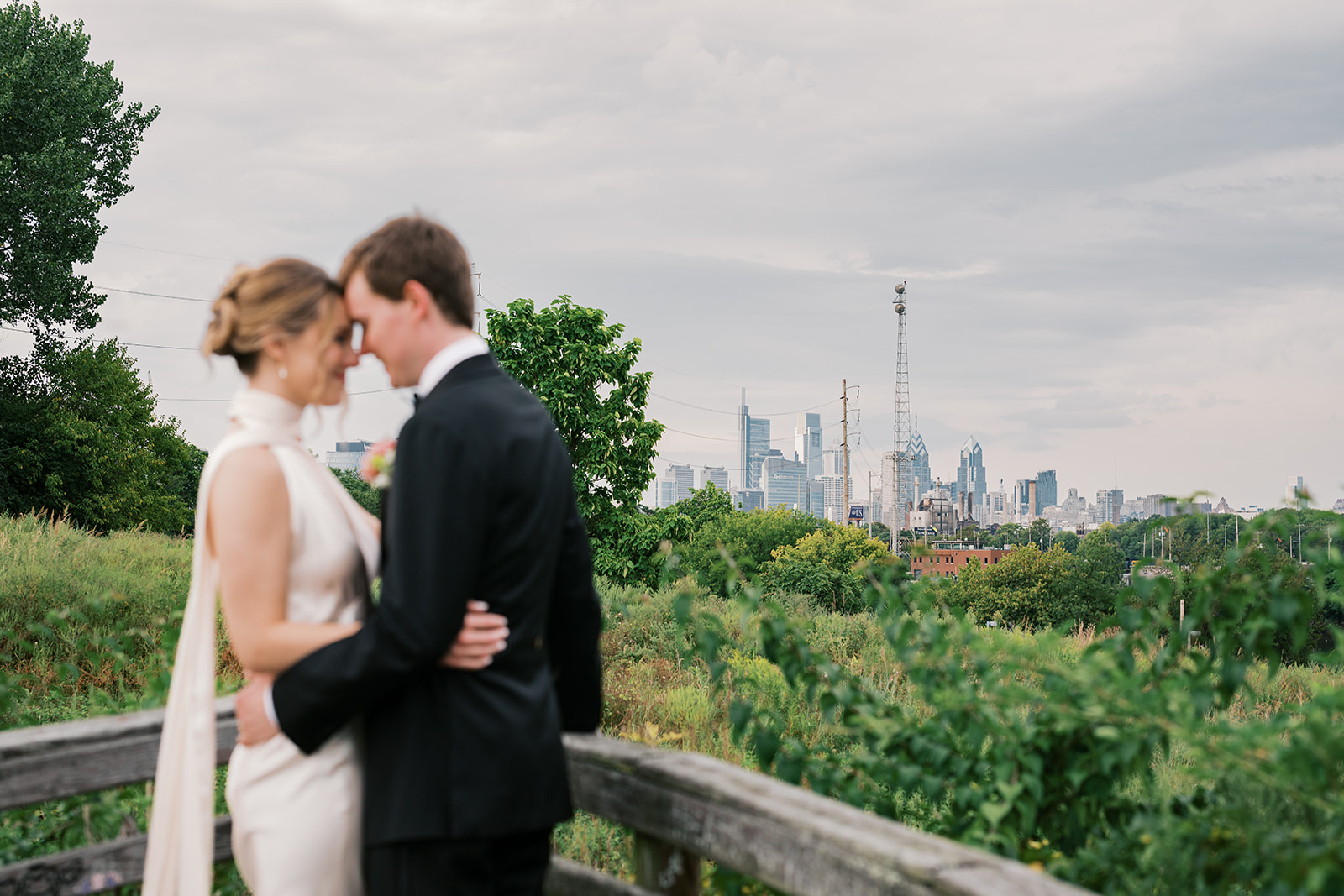 Bride and groom hug each other in front of the Philadelphia skyline during their wedding portraits at Bartram's Garden by Lindsey Ford Photography