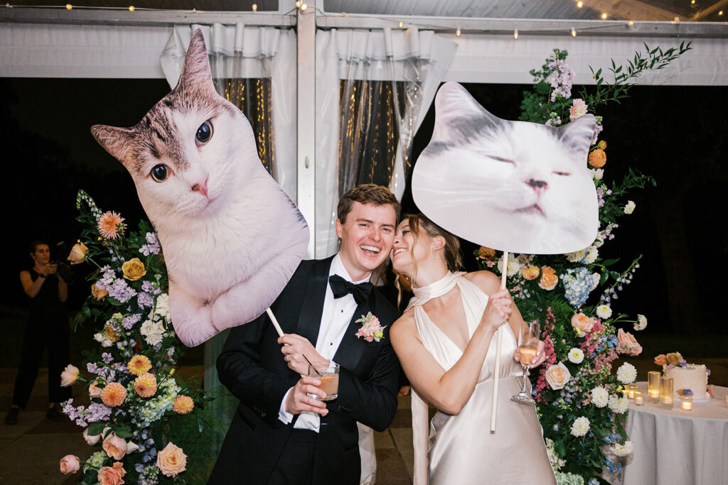 Bride and groom beam as they carry life size cutouts of their cats at their wedding tent reception at Bartram's Garden in Philadelphia