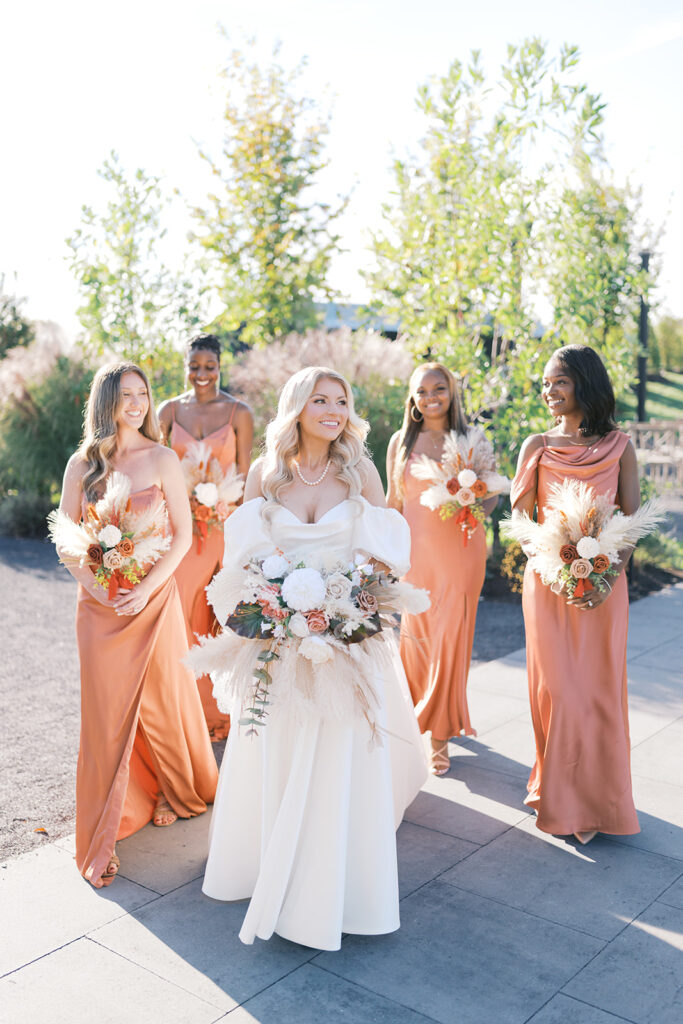 Group of four bridesmaids in rust colored satin bridesmaid dresses from Birdy Grey surround the bride in a white puff sleeve dress from Daydream Bridal in Philadelphia