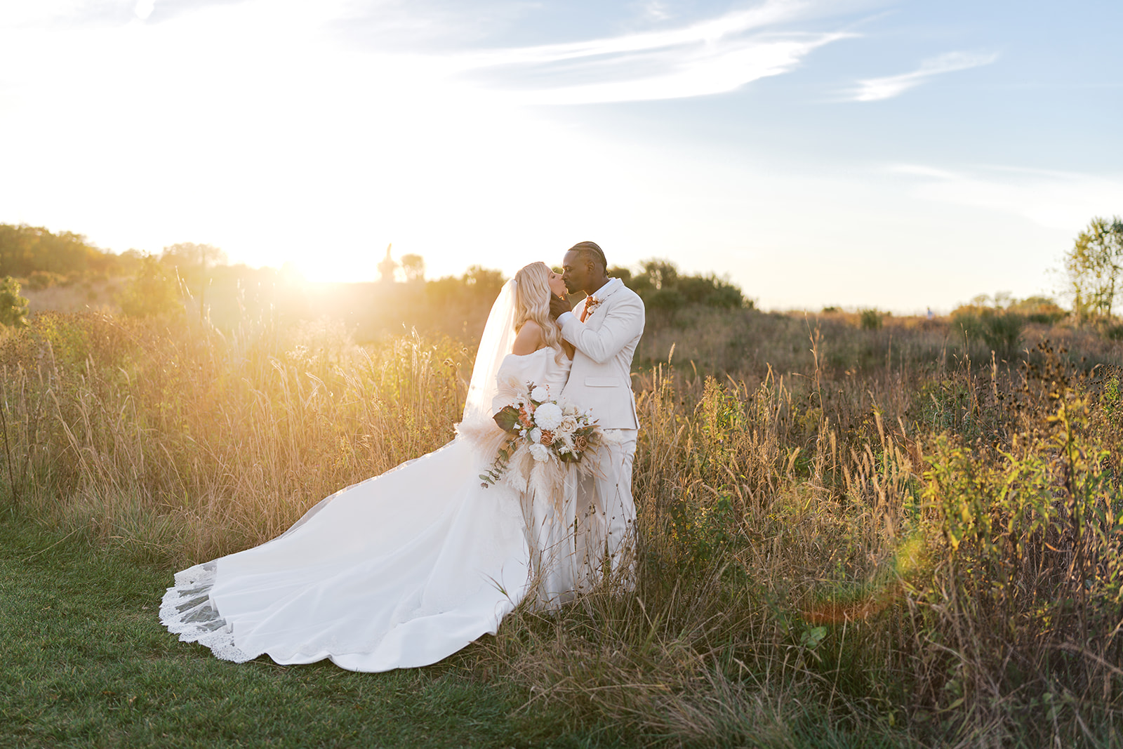 Bride and groom stand and kiss in a green field at sunset during their wedding portraits at Terrain Gardens at DelVal