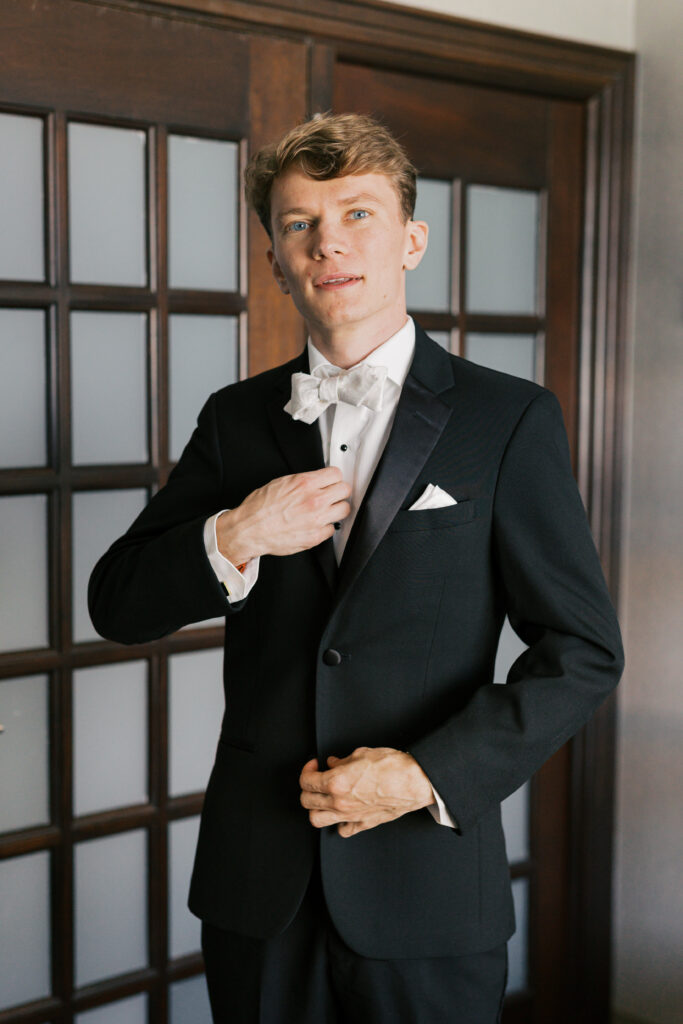 Groom adjusts his shirt underneath a black tuxedo