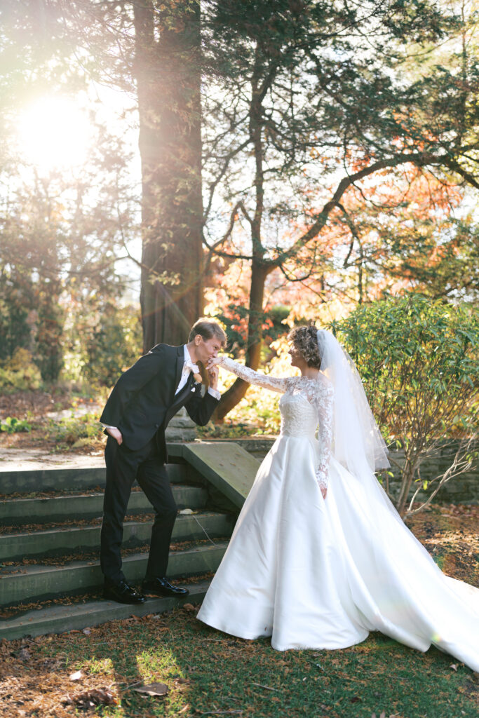 Groom kisses brides hand on a set of stone steps at Stoneleigh gardens during their first look portraits