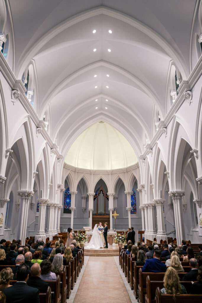 Grand view of a Villanova Church wedding ceremony from the back of the sanctuary featuring soaring Gothic arches and architecture
