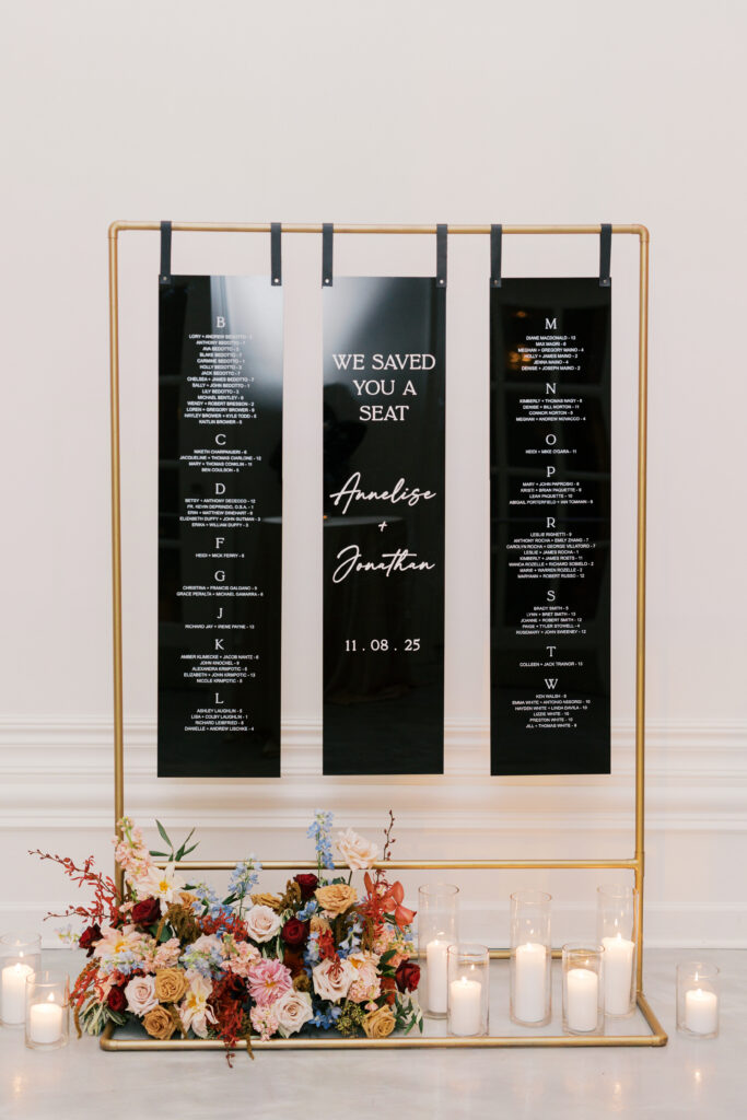 Modern acrylic black and white seating chart hangs on a brass rack accented by fall florals and votive candles