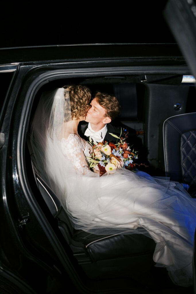 Bride and groom kiss in the backseat of a black town car