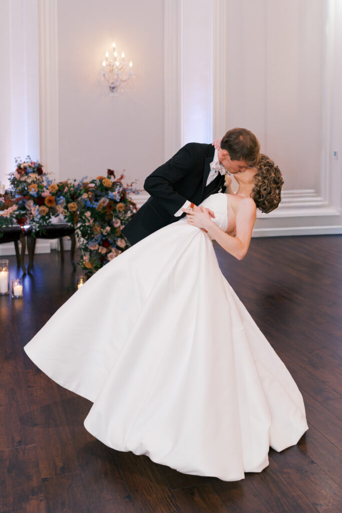 Groom dips bride to kiss her on the dancefloor during their first dance at The Ballroom at Ellis Preserve
