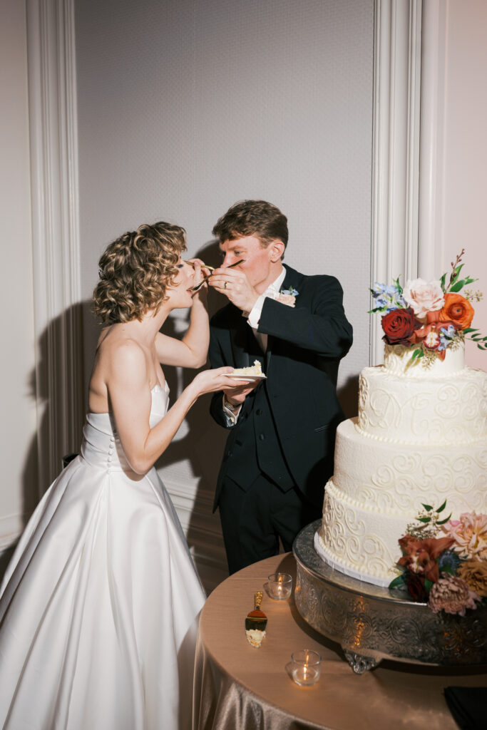 Groom feeds bride a bite of cake during their wedding cake cutting at their Ballroom at Ellis Preserve reception