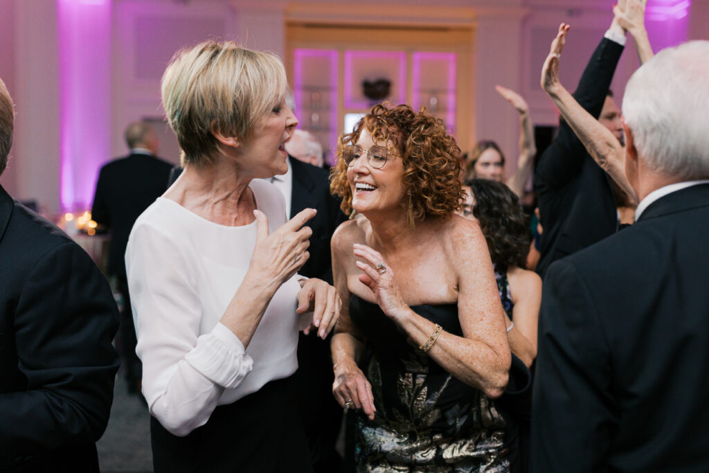 Two women laugh and dance together during a wedding reception at The Ballroom at Ellis Preserve