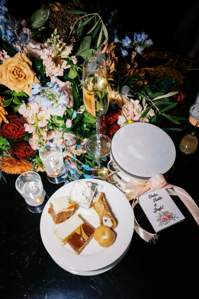 Editorial style flash photo of a dessert plate full of sweet treats next to a lush floral arrangement, wine glass, and glass votive candles