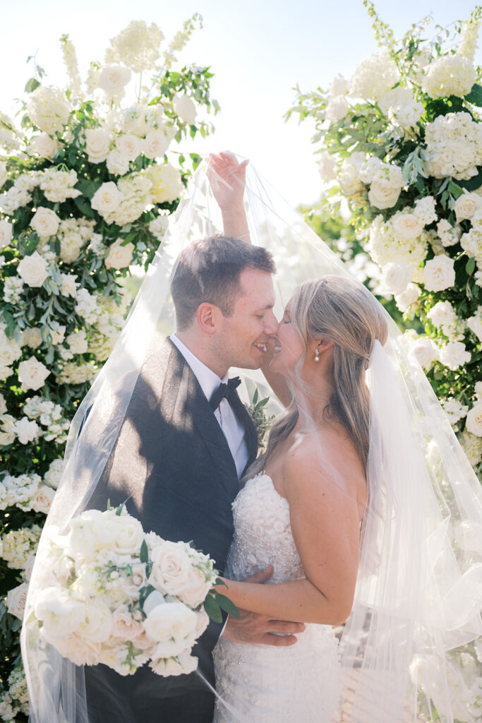 Romantic veil portrait couple kiss under white floral ceremony arch Lake House Inn lakefront Pennsylvania