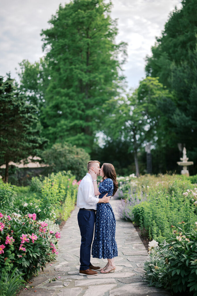 Couple sharing a kiss on the stone garden path surrounded by blooming peonies at their Marian Coffin Gardens engagement session