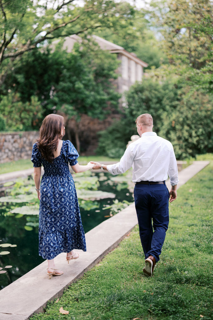 Couple walking hand in hand along the edge of the lily pond at their Marian Coffin Gardens engagement session
