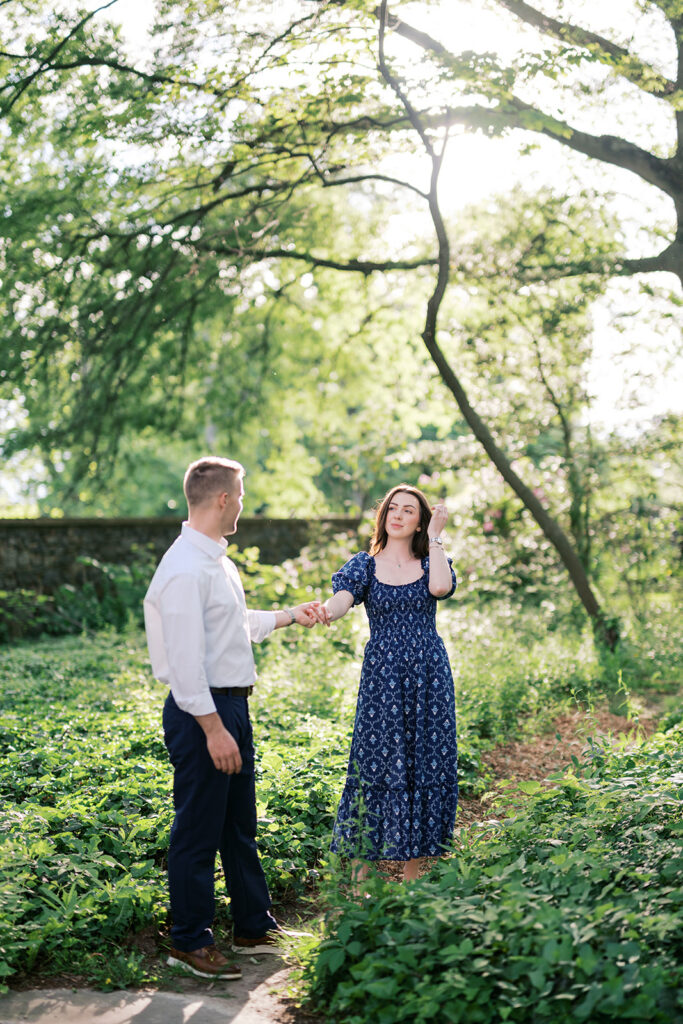 Couple holding hands in sun-dappled wild garden path during golden hour engagement photos