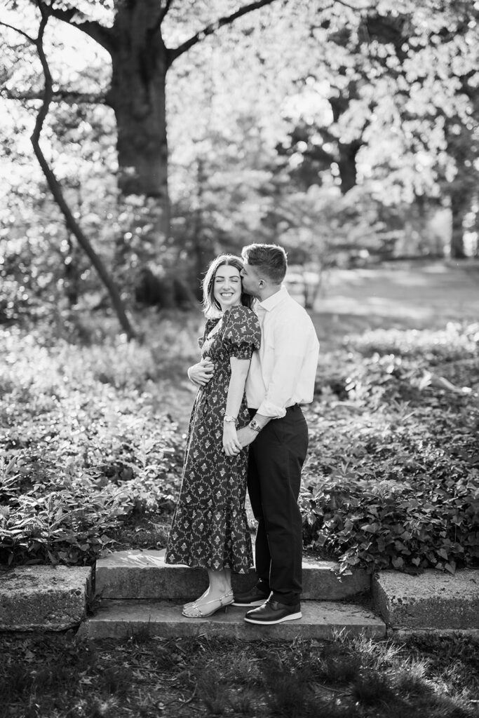 Black and white photo of couple sharing a kiss on stone garden steps surrounded by lush greenery
