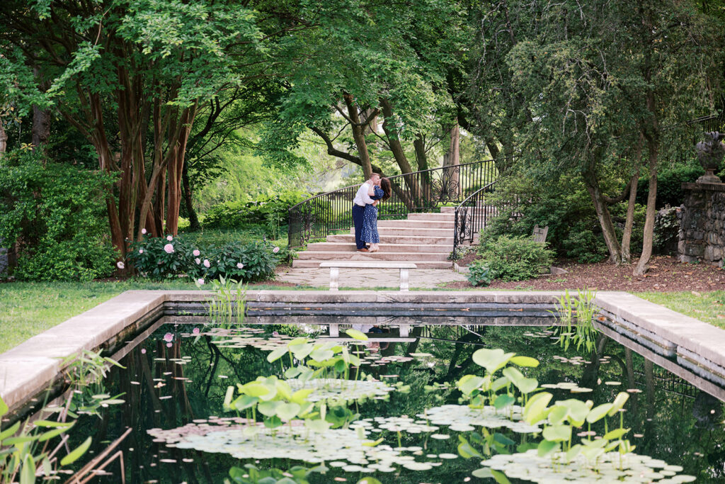Couple kissing on the stone staircase with their reflection in the lily pond below during engagement session at Marian Coffin Gardens in Delaware
