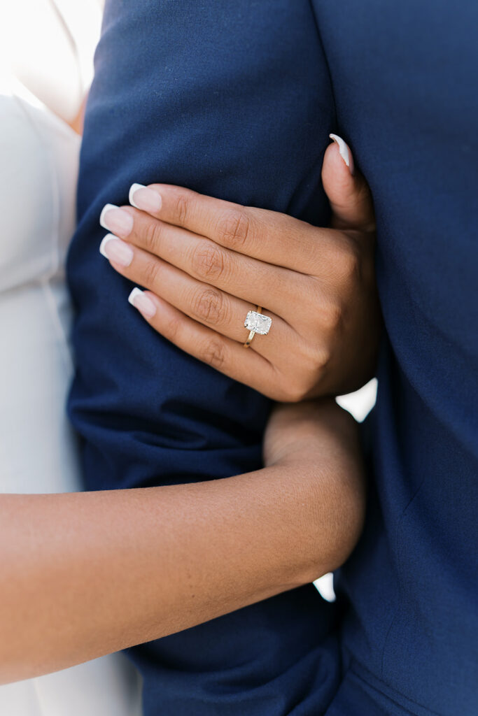Engagement rings close-up emerald cut solitaire diamond on gold band with french manicure at Nemours Estate engagement session Wilmington Delaware