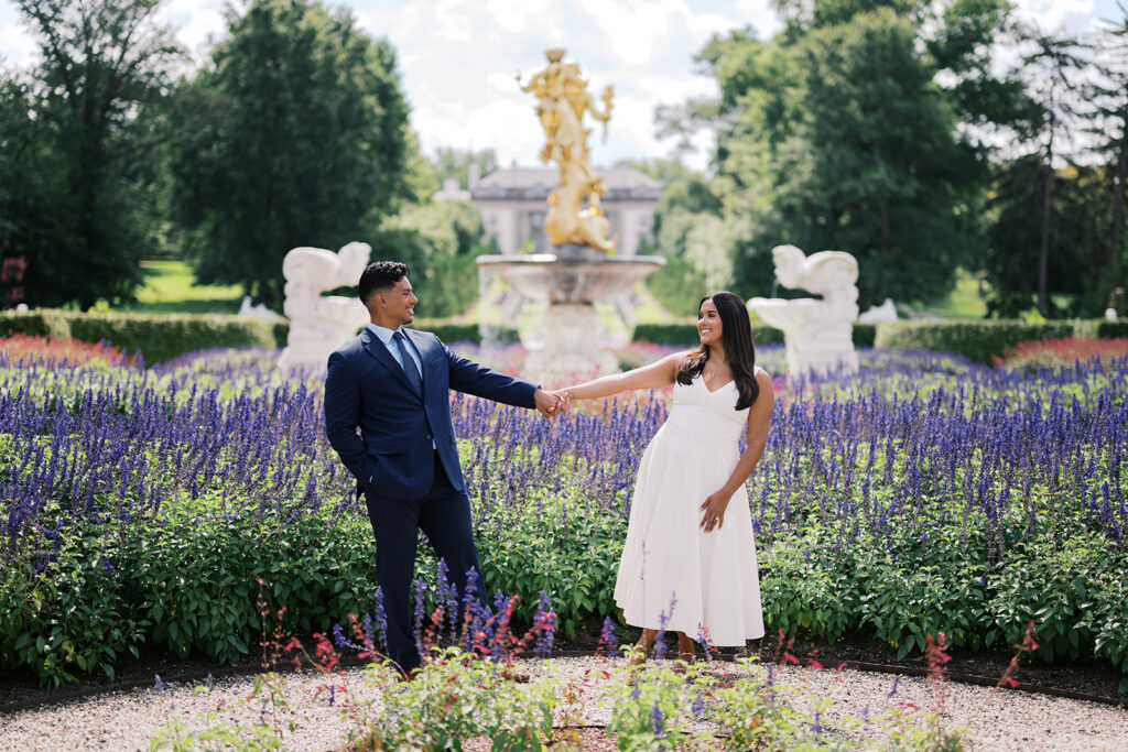 Couples photoshoot outfits summer white midi dress and navy suit holding hands in Nemours Estate Delaware flower garden engagement photos