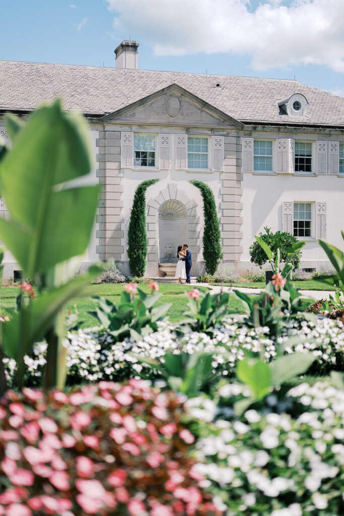 Nemours Estate engagement session couple kissing framed by cypress trees and lily pond at Nemours carriage house garden Wilmington Delaware