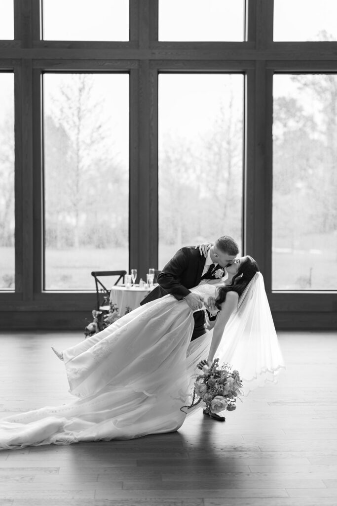 Black and white photo of a groom dipping his bride for a kiss before the tall reception windows at Westwynd Gardens in Honey Brook, PA