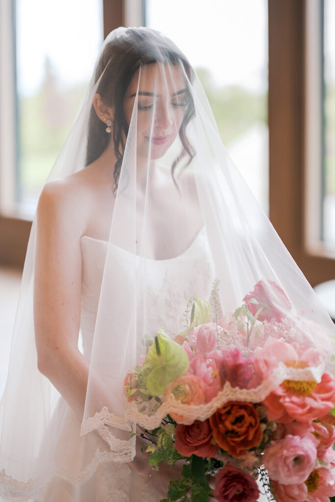 Bride with her veil draped over her face holding a coral peony and green anthurium bouquet