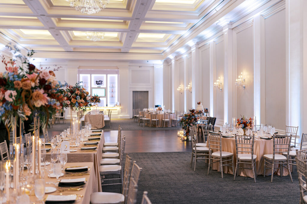 Large ballroom with uplighting on the walls is decorated with banquet style and round reception tables