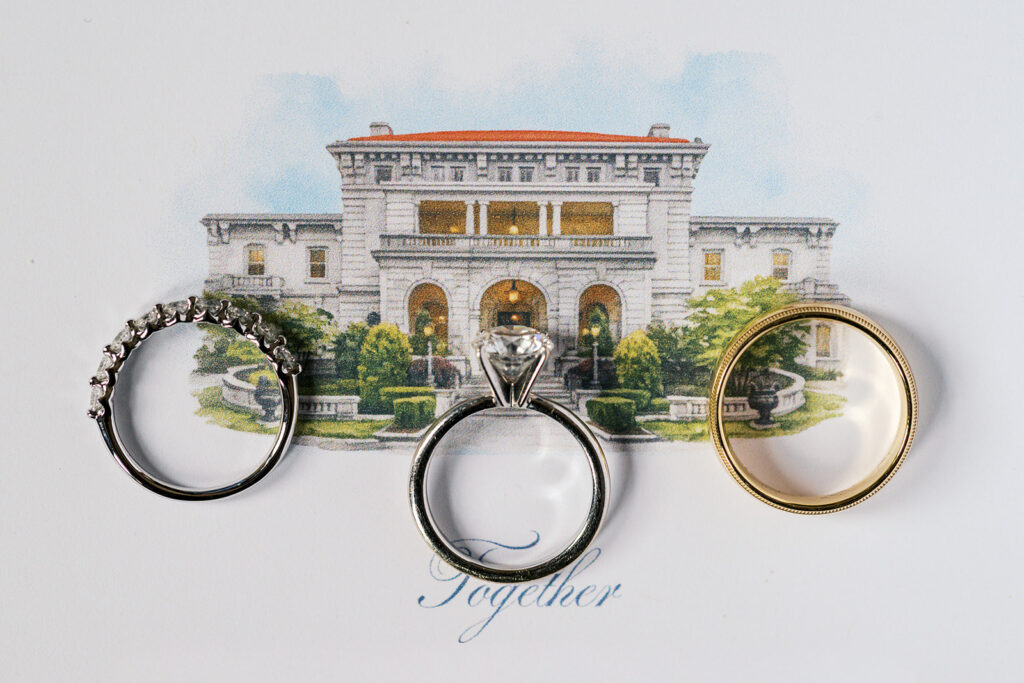 Wedding rings resting on a watercolor illustration of Elstowe Manor at the Elkins Estate