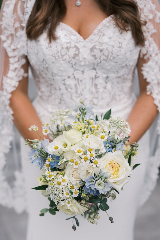 Bride in a lace gown holding a blue, white, and yellow summer bouquet at her Elkins Estate wedding