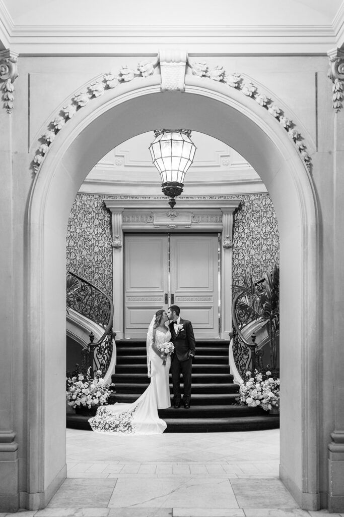 Bride and groom kiss at the base of a grand staircase framed by an arched doorway at Elkins Estate wedding venue in Philadelphia, photographed by Lindsey Ford