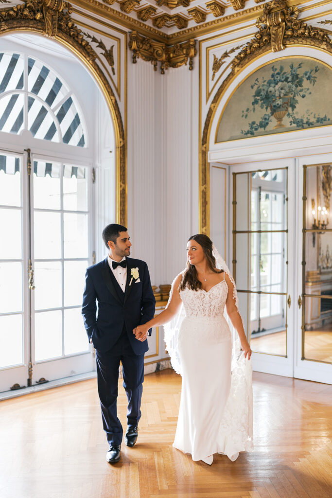 Bride and groom walk hand in hand inside the gilded music room at Elstowe Manor, Elkins Estate in Philadelphia, PA