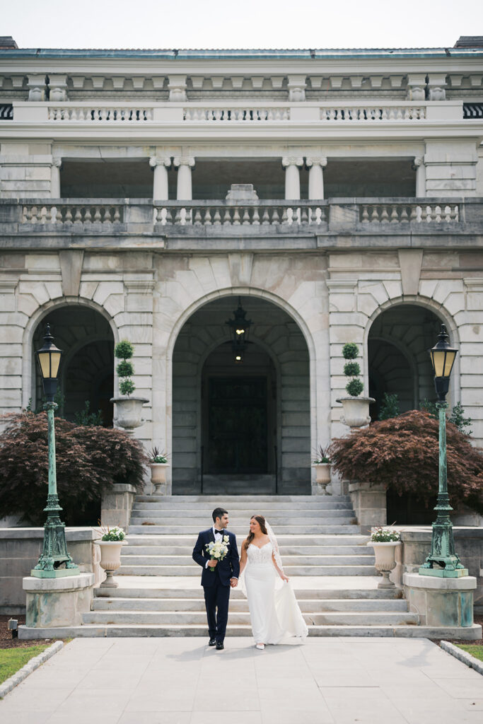 Bride and groom walk hand in hand in front of Elstowe Manor at Elkins Estate in Philadelphia, photographed by Lindsey Ford