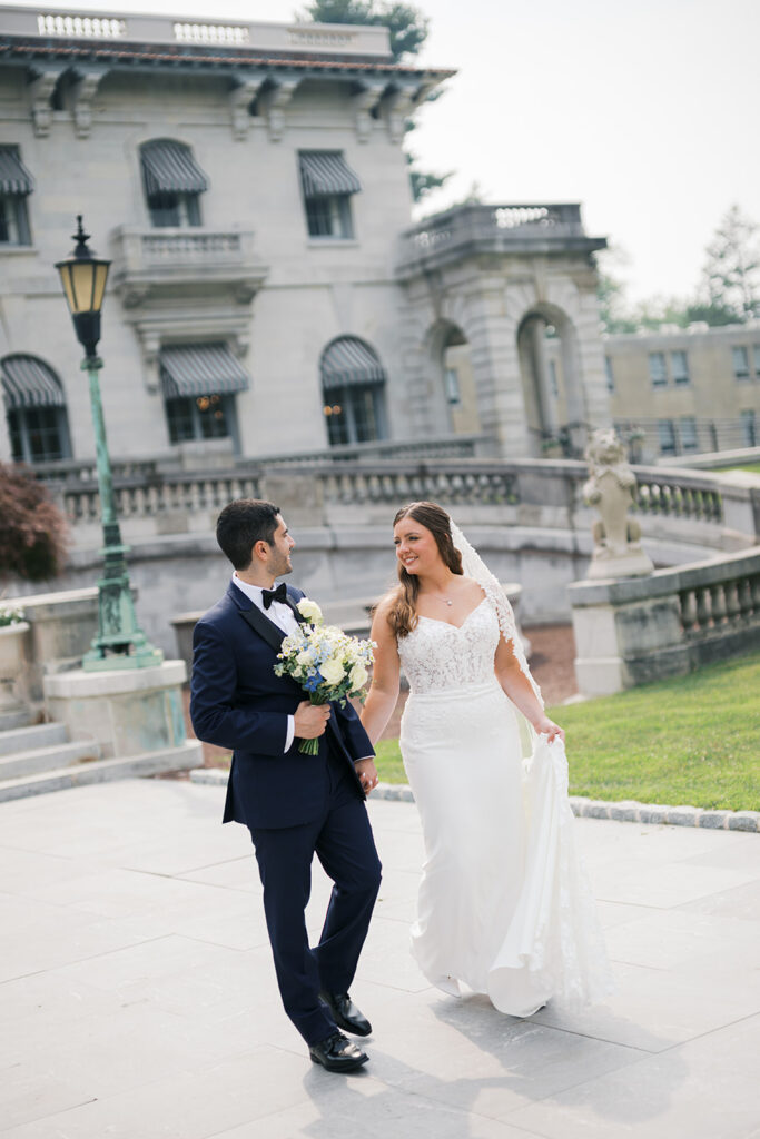Bride and groom walk hand in hand in front of Elstowe Manor at Elkins Estate in Philadelphia, photographed by Lindsey Ford
