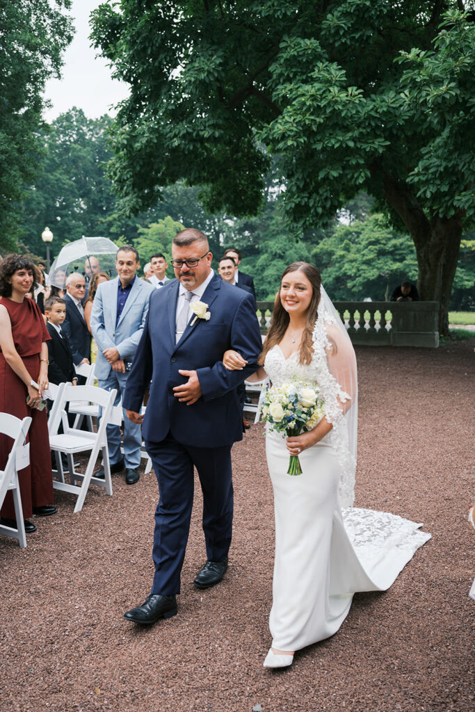 Bride's father walks bride down the aisle of an outdoor Elkins Estate wedding ceremony