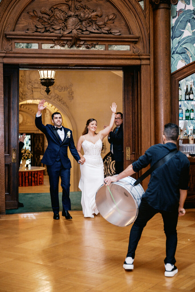 Bride and groom enter their reception with raised hands to a traditional Zaffa drummer